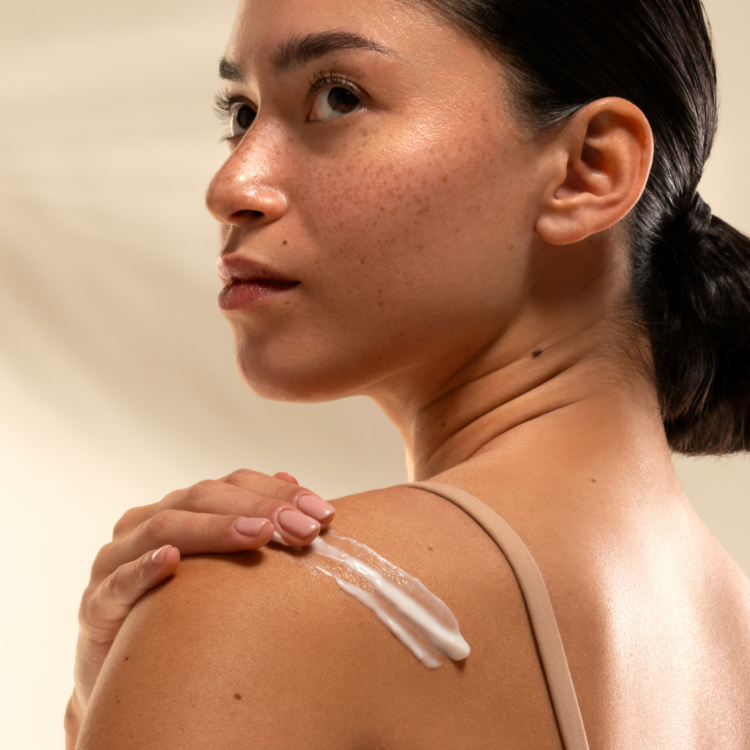 Woman applying cream to her shoulder against a neutral background